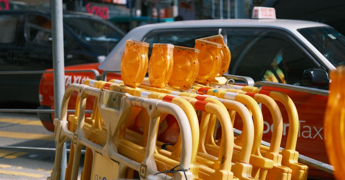 Traffic barriers with yellow lights in a city street with taxis in the background.