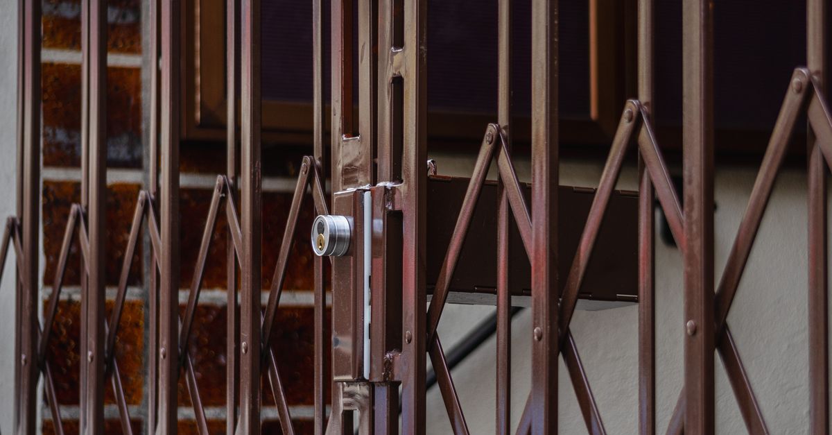 Close-up of a rusty folding metal gate with a lock, showing its design and texture.