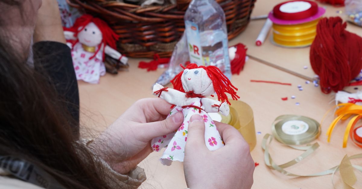Person crafting a floral dress rag doll using colorful materials and threads.