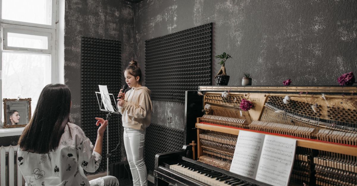 A young girl takes a vocal lesson in a soundproof music studio with her teacher.