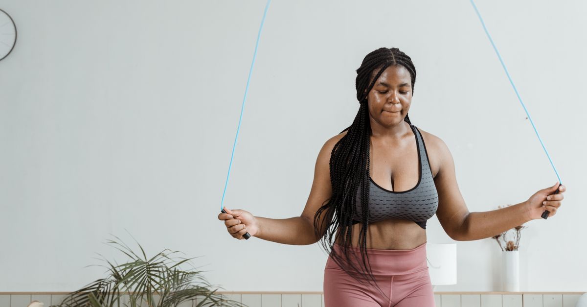 Fit woman in activewear jump roping indoors, promoting fitness and health.