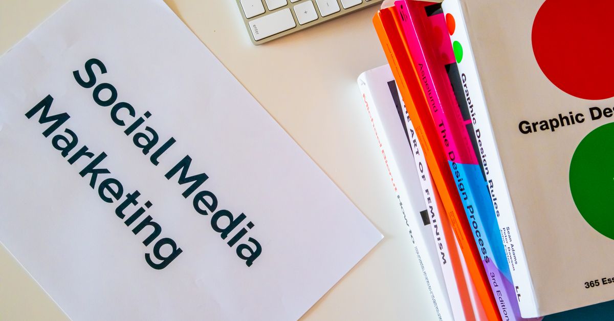 A top view of social media marketing text alongside graphic design books and a keyboard.