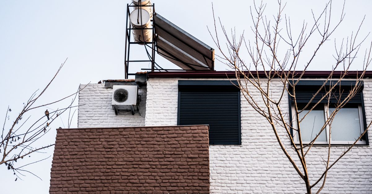 A minimalist building facade with air conditioner and bare winter trees, viewed from a low angle.