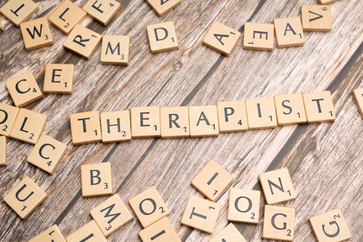 Wooden letter tiles on a rustic surface spell the word 'Therapist'.