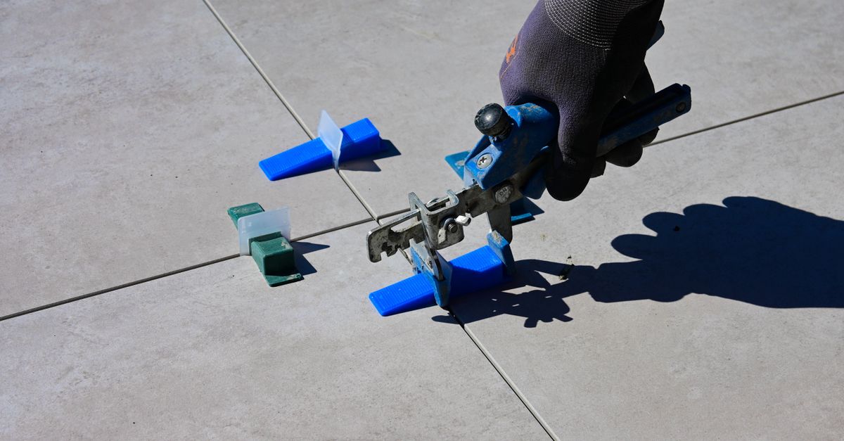 A gloved hand using a leveling tool to install tiles with spacers.