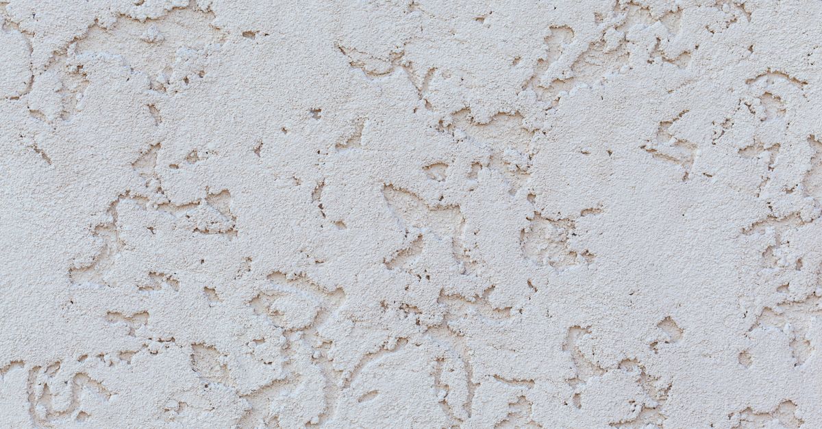 Textured background of white plaster wall with small holes on surface of building