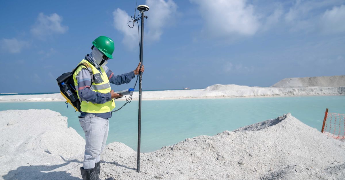 Surveyor in protective gear conducting measurements by a remote beach with GPS equipment.