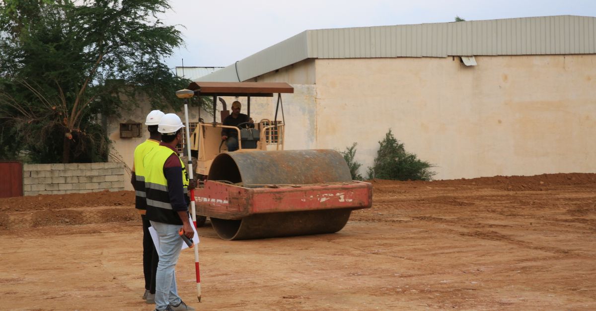 Engineers in high-visibility vests supervise road construction with a roller.