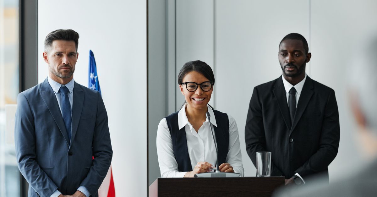 Diverse leaders at a conference podium with US flag in the background.
