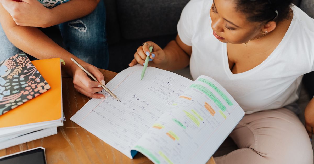 Two adults collaborate on educational content with notebooks and pens indoors.