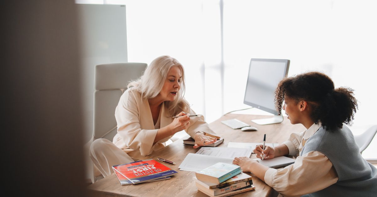 Educator explains concepts to a student in a classroom environment with books and notes.