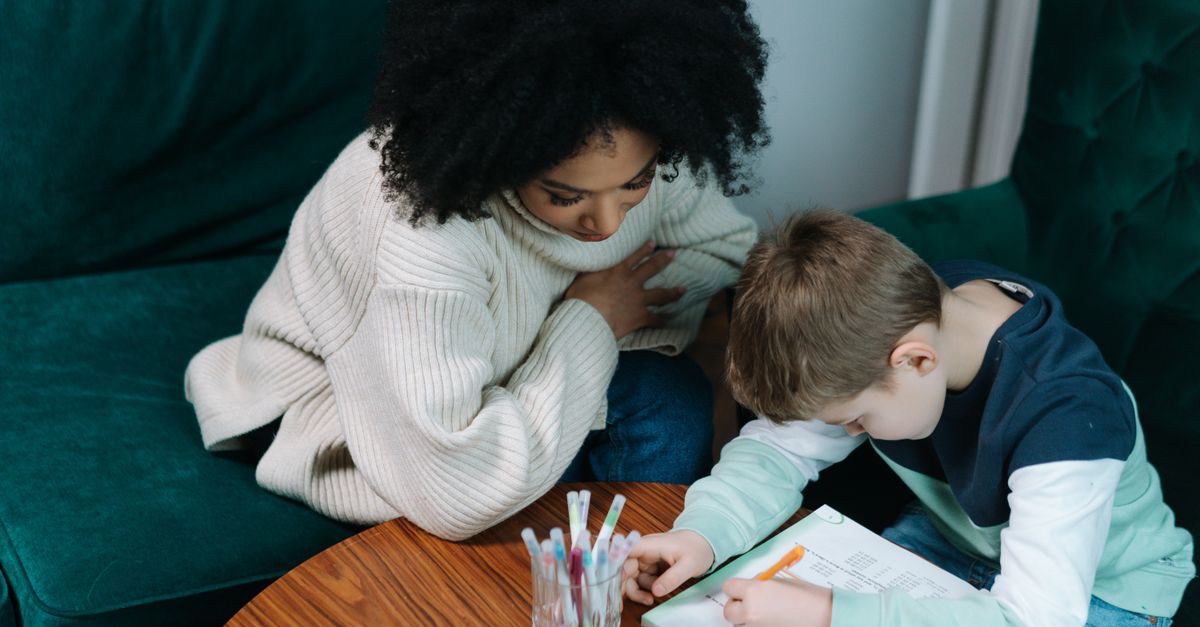 A child being tutored at home, writing in a notebook while seated on a green couch.