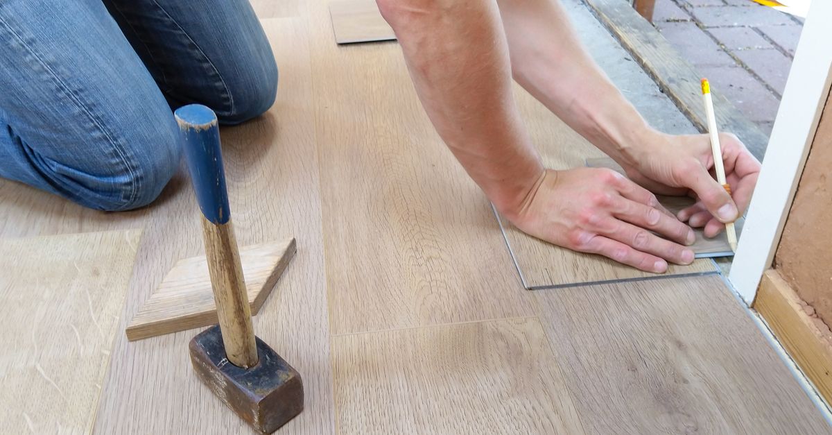 A craftsman carefully measures and marks wooden floor panels for precise installation.