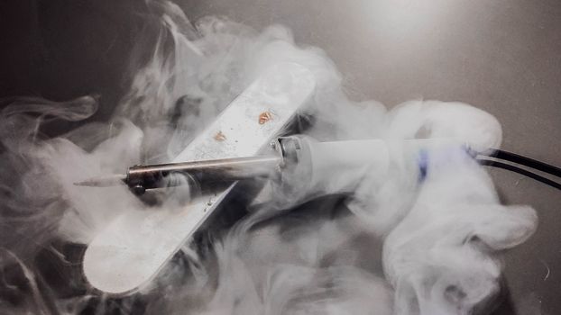 Detailed image of a soldering iron emitting smoke, showcasing its heated tip and white fumes.