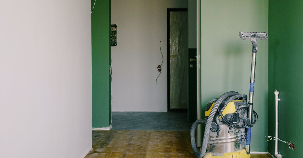 Industrial vacuum cleaner placed on dirty parquet in room with green walls and doorway in spacious apartment during repair works