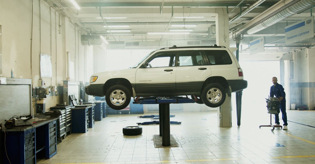 Mechanic repairing a car on a lift in a well-equipped garage.