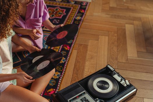 Two people explore vinyl records beside a vintage turntable on wooden flooring.