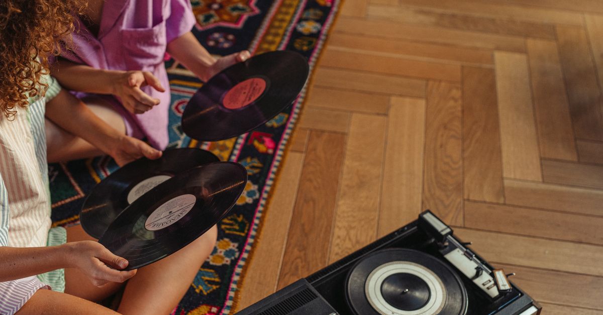 Two people explore vinyl records beside a vintage turntable on wooden flooring.