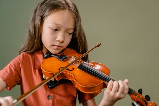 A young girl intensely focused on playing the violin indoors with a warm, artistic tone.