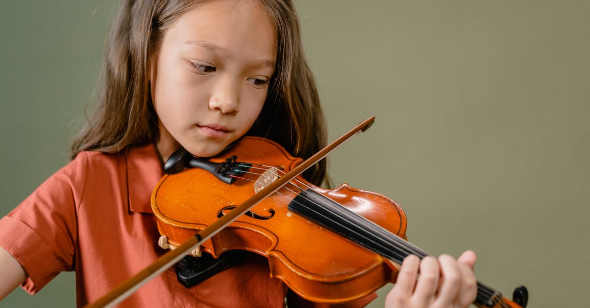 A young girl intensely focused on playing the violin indoors with a warm, artistic tone.