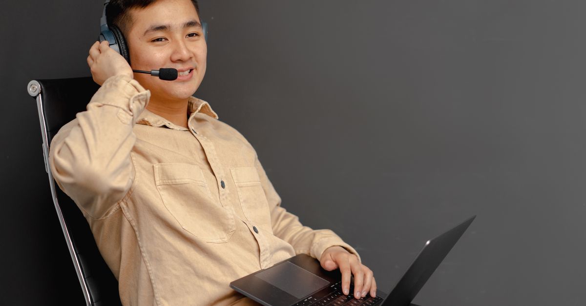 Smiling customer service agent using a laptop and headset indoors.