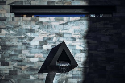 Modern waterfall feature on patterned stone wall with abstract design and triangle shape.