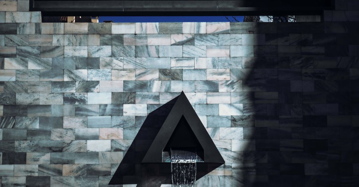 Modern waterfall feature on patterned stone wall with abstract design and triangle shape.