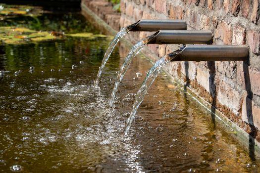 Crystal clear water streams from a modern stainless steel fountain into a serene outdoor pond.