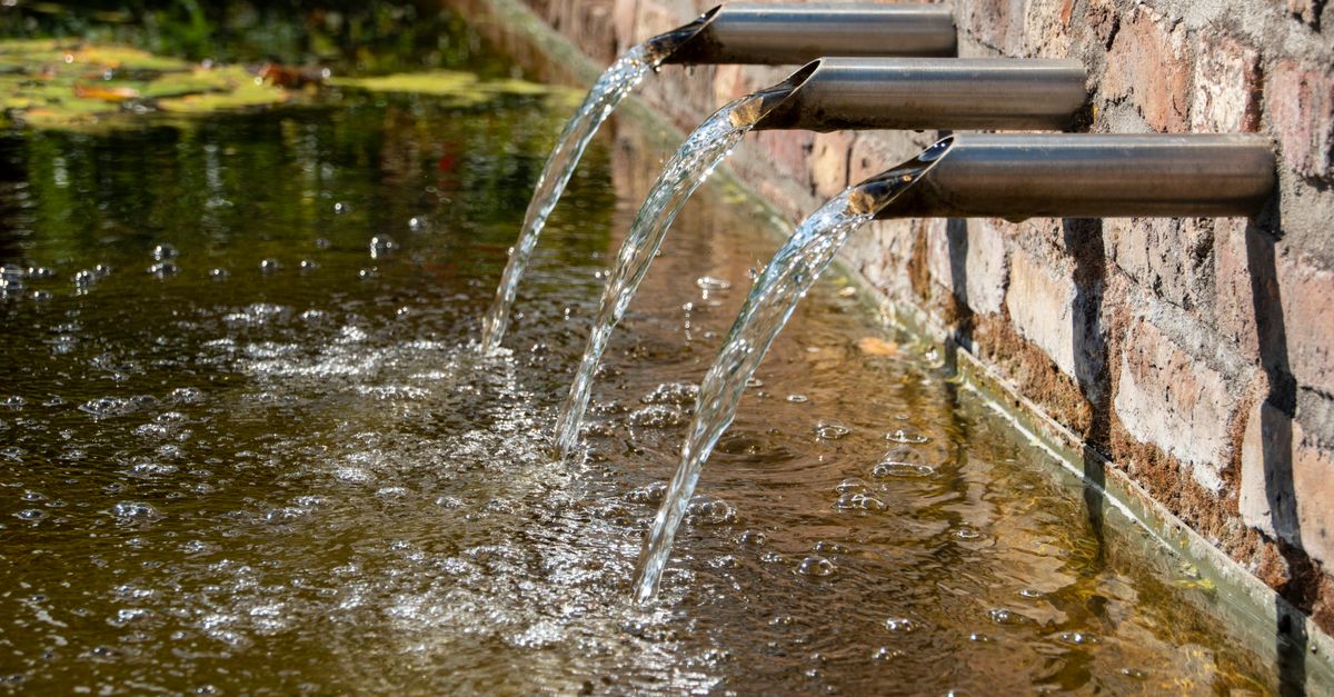 Crystal clear water streams from a modern stainless steel fountain into a serene outdoor pond.