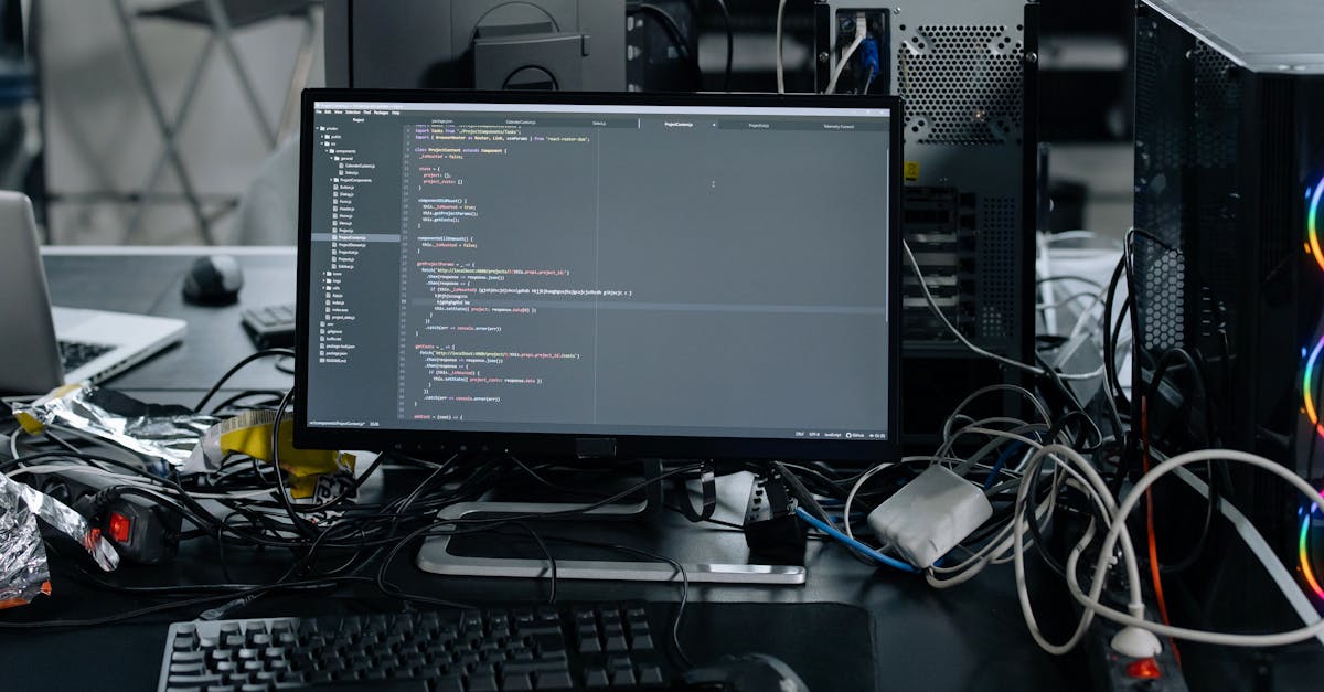 A cluttered workstation in an office featuring a monitor displaying code, surrounded by a keyboard, mouse, and wiring.