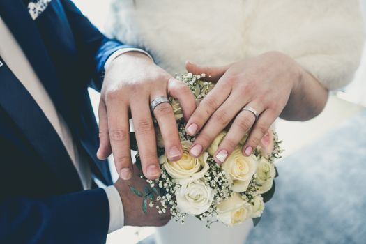 Intimate close-up of a newlywed couple's hands showcasing wedding rings with a white rose bouquet.