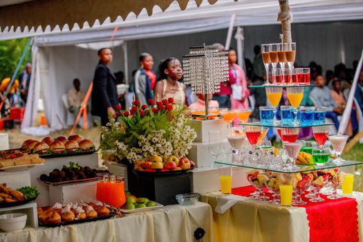 Elegant outdoor buffet setup with vibrant drinks and food at a wedding event.