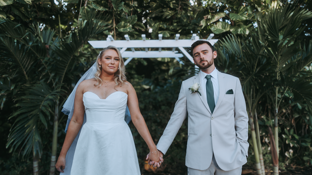 A bride and groom holding hands under a white arch in an outdoor wedding setting.