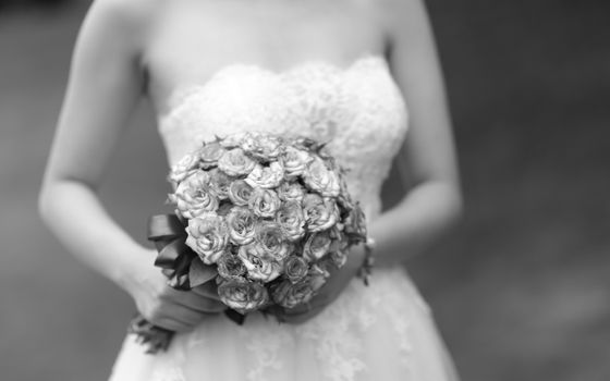 Close-up of a bride holding an elegant floral bouquet in grayscale.