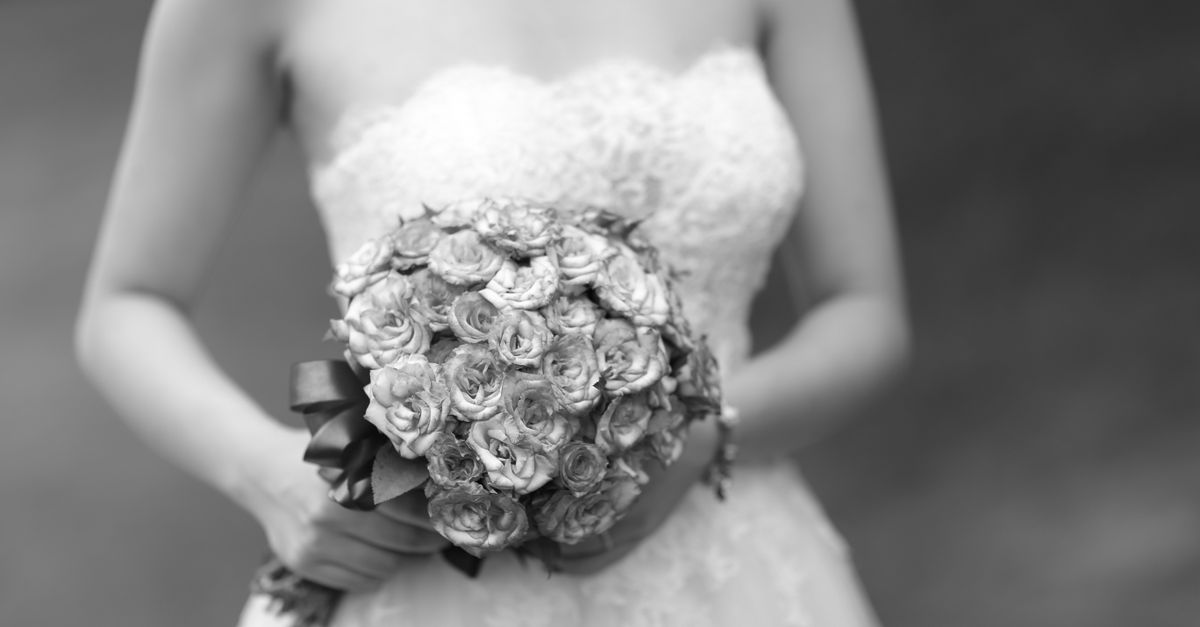 Close-up of a bride holding an elegant floral bouquet in grayscale.