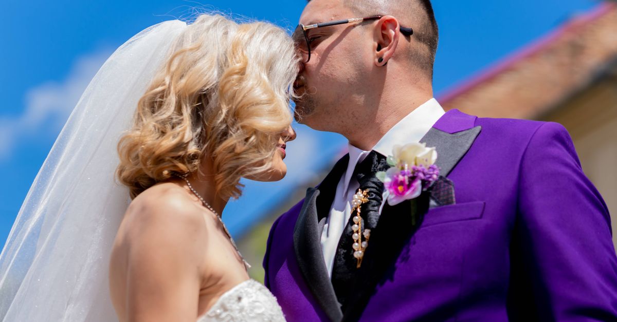 A romantic wedding moment captured with the couple sharing a tender kiss under a clear blue sky.