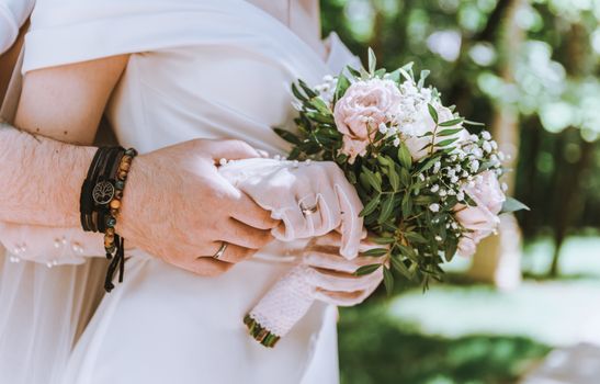 Close-up of a bride and groom holding a floral bouquet, symbolizing love and marriage.