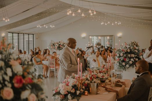Beautiful indoor wedding reception with floral arrangements and guests enjoying a speech.