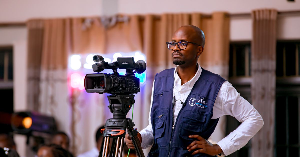 A focused cameraman operates a video camera indoors, capturing an event.