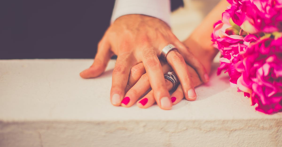 Close-up of a married couple's hands with wedding rings and pink flowers, symbolizing love and commitment.