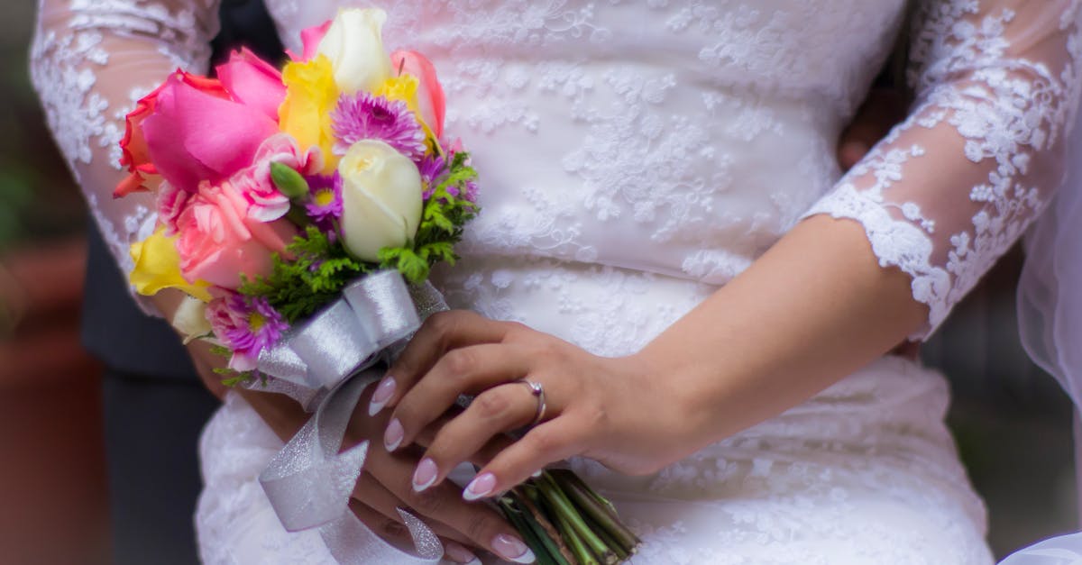 A close-up of a bride in a lace dress holding a vibrant wedding bouquet.