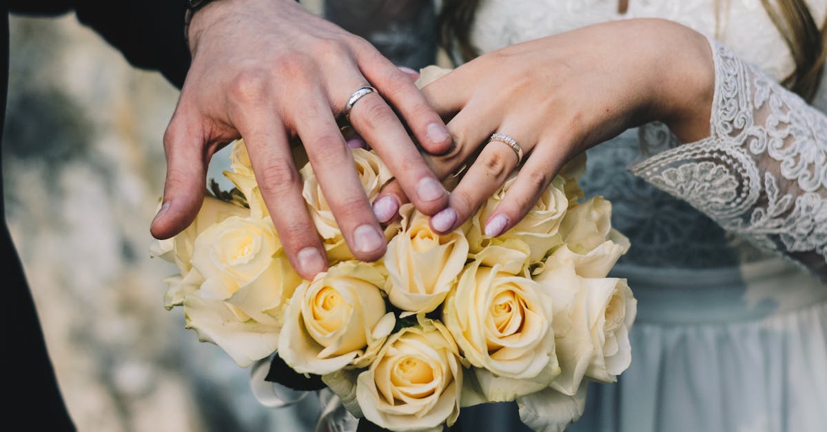 Close-up of a couple's hands displaying wedding rings above a bouquet of yellow roses.