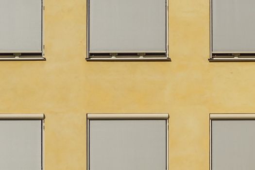 Modern building facade in Oslo with minimalist ochre walls and closed blinds creating a geometric pattern.