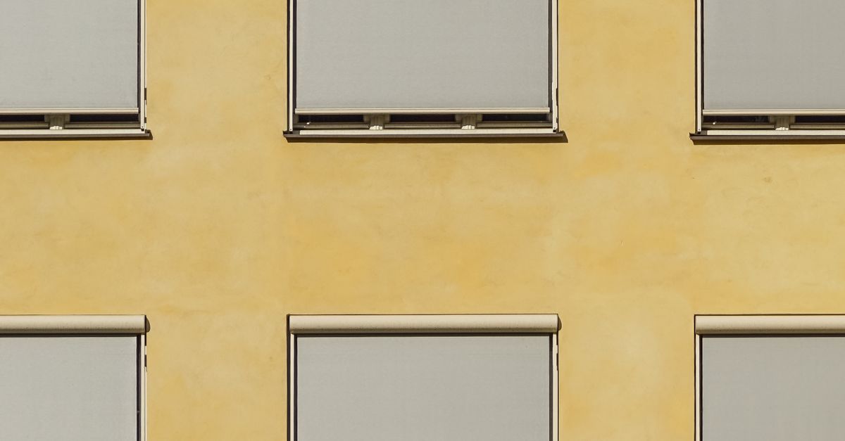 Modern building facade in Oslo with minimalist ochre walls and closed blinds creating a geometric pattern.