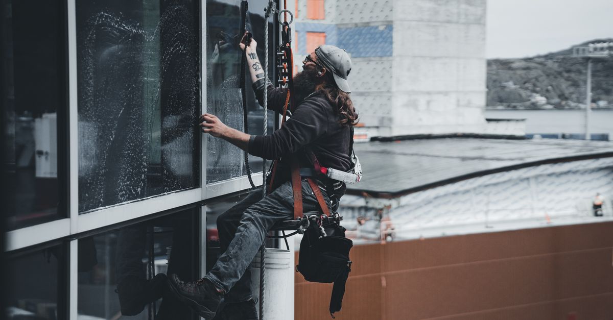 A man cleaning skyscraper windows with a harness, showcasing urban high-rise work.