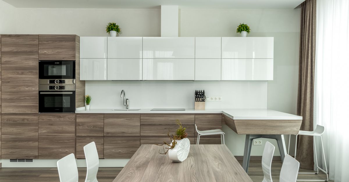 Modern open plan kitchen with white glossy and wooden cabinets and dining table with white chairs near in light apartment