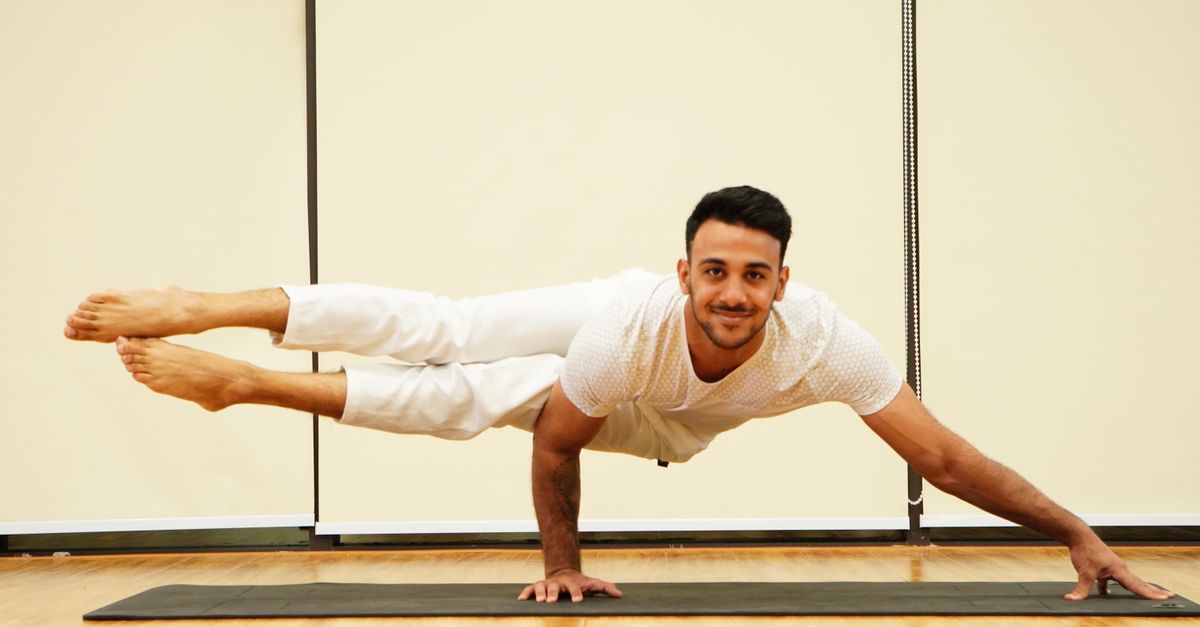 A man balances in an advanced yoga pose on a mat indoors, showcasing strength and focus.